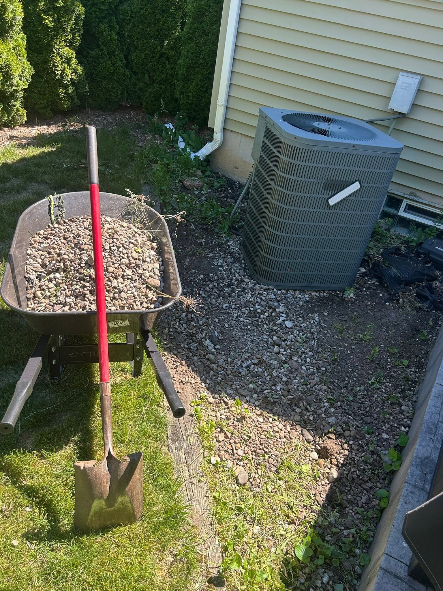 Wheelbarrow filled with landscape rock beside a residential side yard during rock and gravel removal.