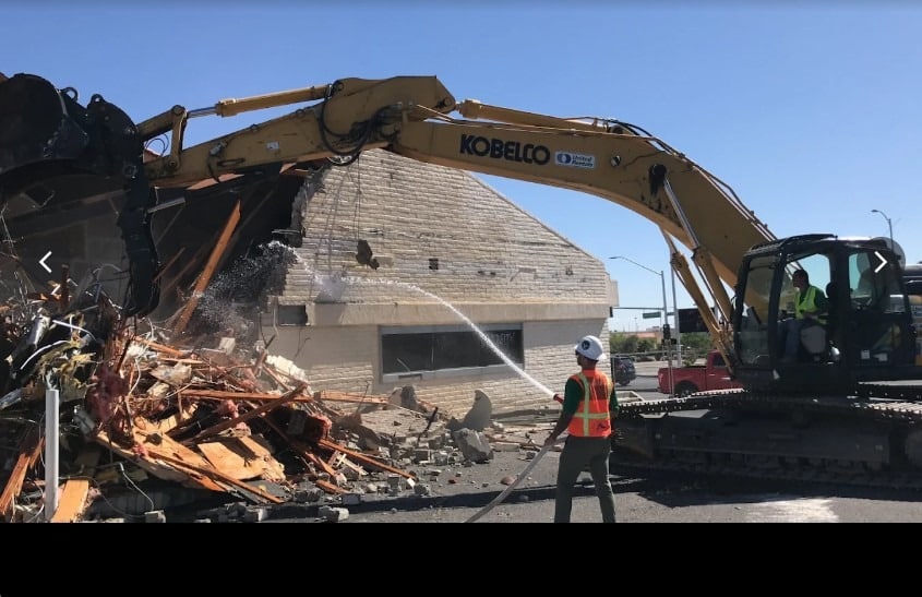 Construction debris removal at a Las Vegas demolition site with an excavator, broken lumber, concrete, and masonry debris.